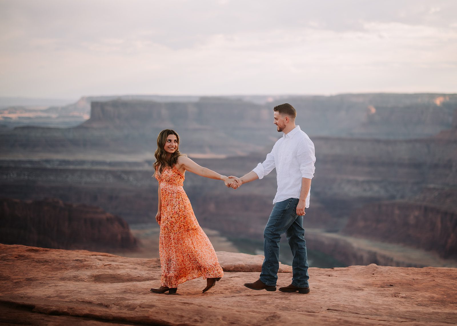 Couple posing during an engagement photography and videography session at Dead Horse State Park near Moab, Utah, with breathtaking views of Canyonlands National Park and Arches National Park in the background, capturing the stunning red rock formations and expansive desert landscape. Double Exposure