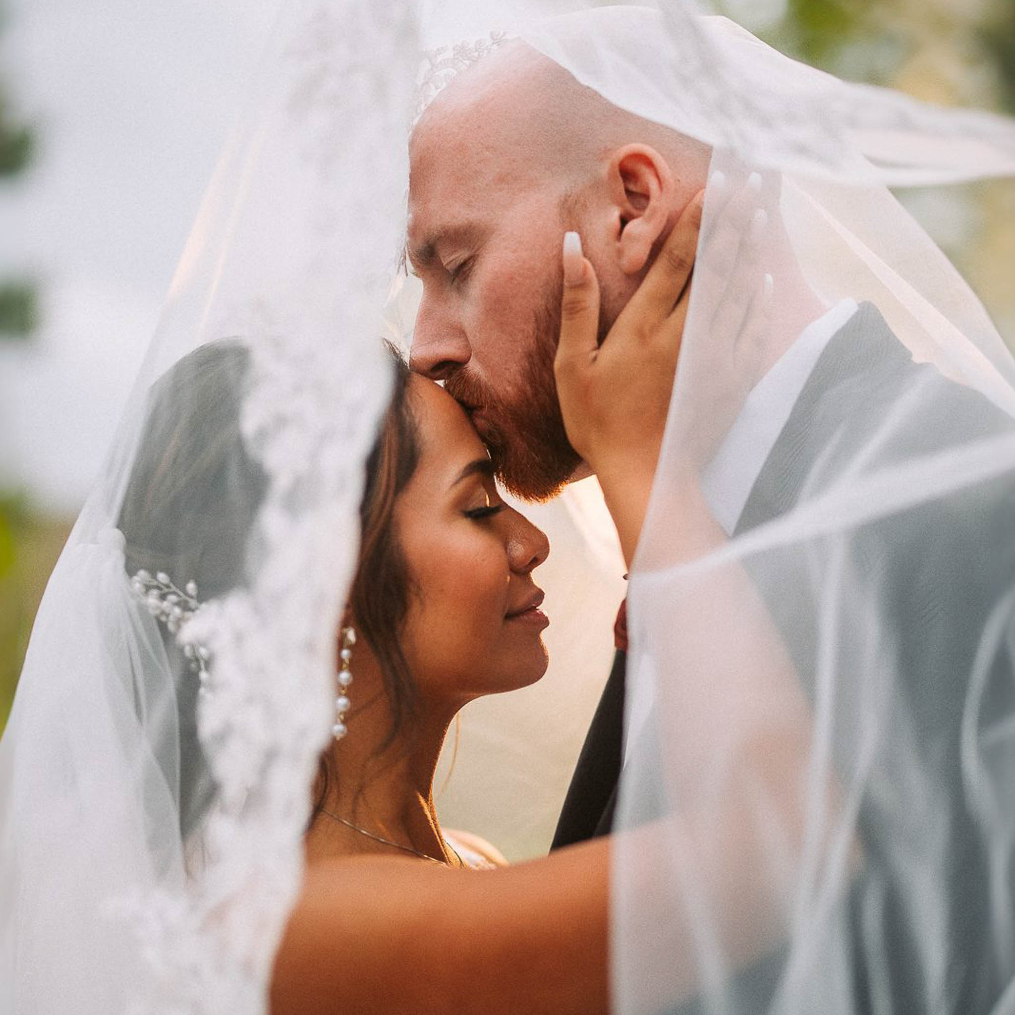 young interracial wedding couple embracing, groom kissing bride's forehead. POV through the veil. Hawkins Photo and Film Utah Wedding Photographer St. George Utah. Destination Photography and Videography