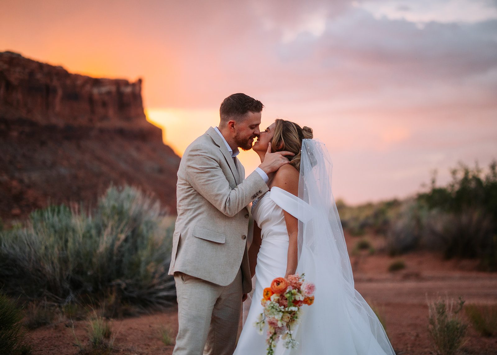 Man and woman embrace in a passionate kiss during golden hour on their wedding day surrounded by redrock cliffs in moab utah shot on canon r6 MII 50mm 1.2