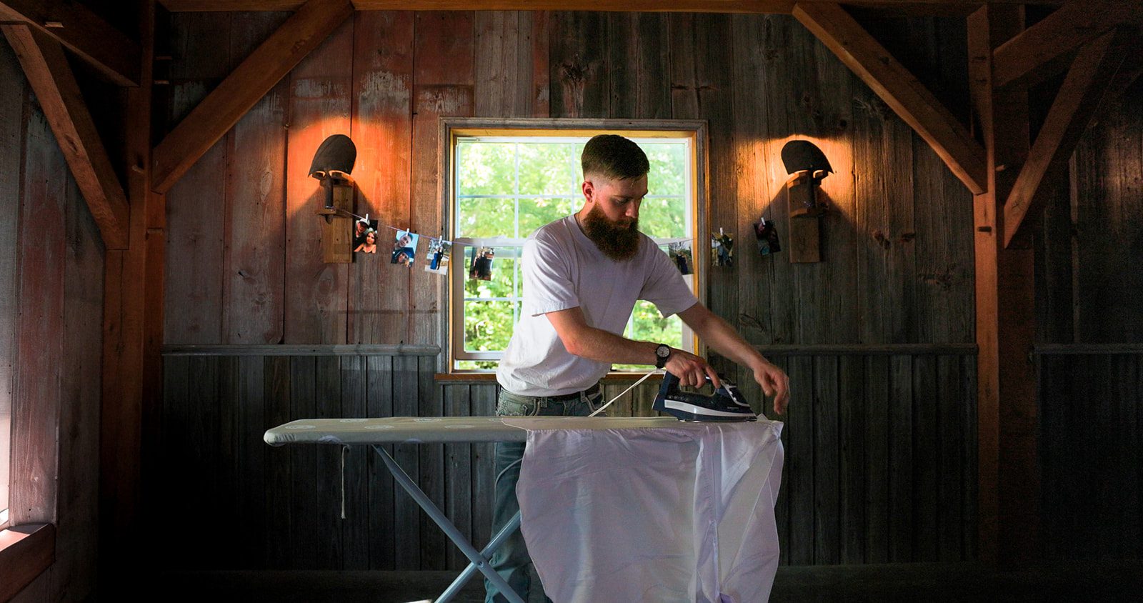 Groom ironing his shirt before the ceremony in a rustic barn with tungsten light in missouri